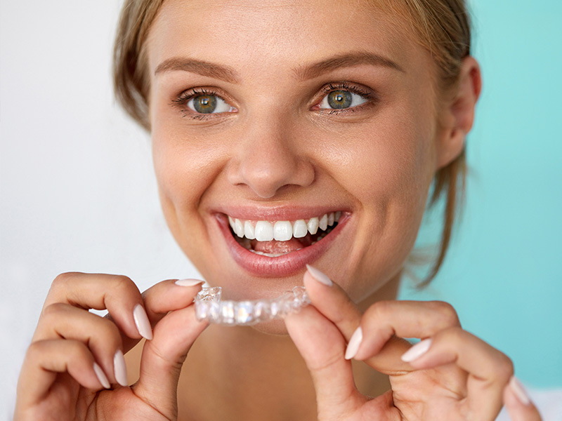 The image shows a woman with a radiant smile holding up a clear dental impression tray, likely to demonstrate its use or to promote dental care products.